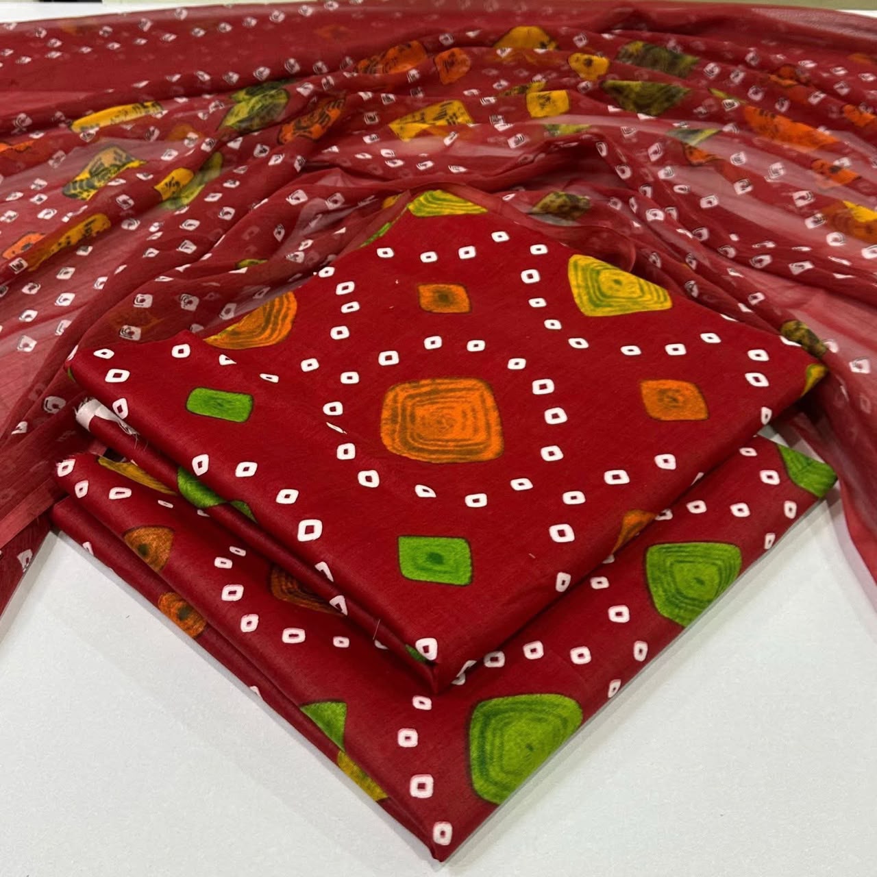 lawn 3 piece suit in  red fwith a white dotted bandhani pattern and green and orange printed motifs