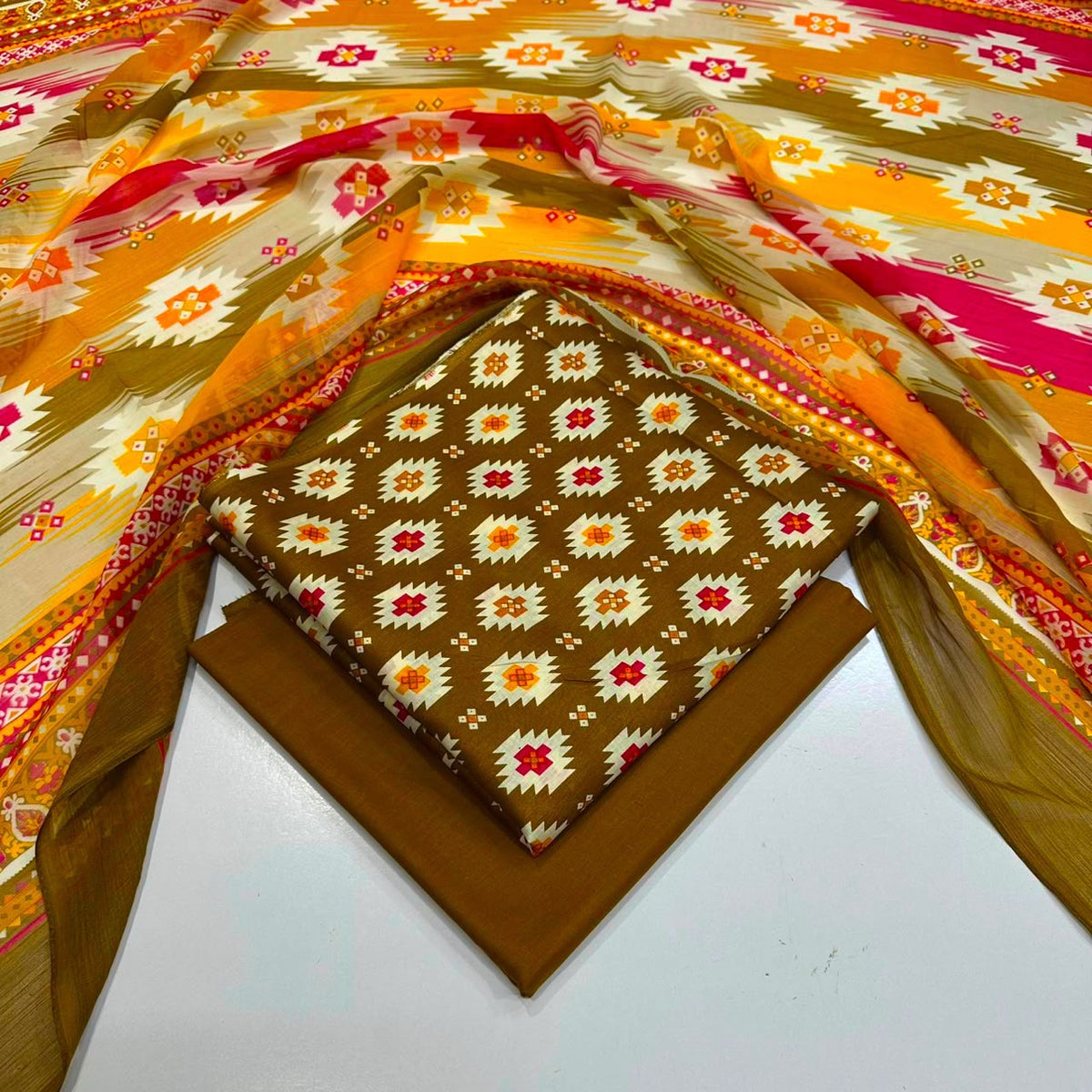 lawn 3 piece suit featuring a brown base with a repeating white, orange, and red floral ikat pattern